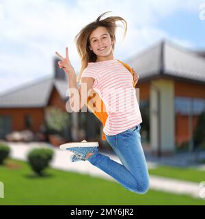 Glückliches Teenager-Mädchen, das in die Nähe des Hauses springt. Schulferien Stockfoto