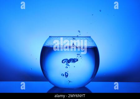 Spritzen Sie Wasser in eine runde Fischschüssel auf blauem Hintergrund Stockfoto