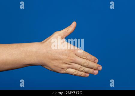 Ein Mann streckt seine Hand aus, um sich die Hand zu schütteln, isoliert auf blauem Hintergrund. Die Hand des Mannes ist bereit für den Handschlag. Stockfoto