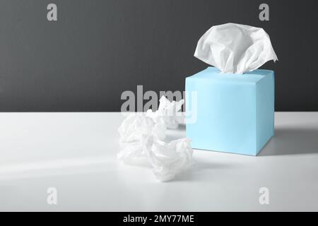 Gebrauchte Papiertücher und blauer Kasten auf dem weißen Tisch. Platz für Text Stockfoto