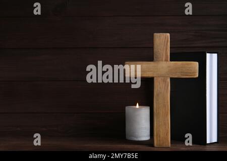 Kreuz, Bibel und brennende Kerze auf Holzhintergrund, Platz für Text. Christliche Religion Stockfoto