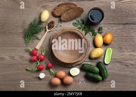 Flache Liegezusammensetzung von Zutaten für Okroshka mit Kvass auf Holztisch. Traditionelle russische Sommersuppe Stockfoto