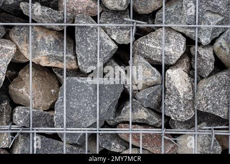 Steinwand aus hellgrauem Schleifstein, umschlossen von einem Metallgitter. Mineralische Oberfläche ohne Mörtelfugen. Bau eines alten Hauses und eines Pa Stockfoto