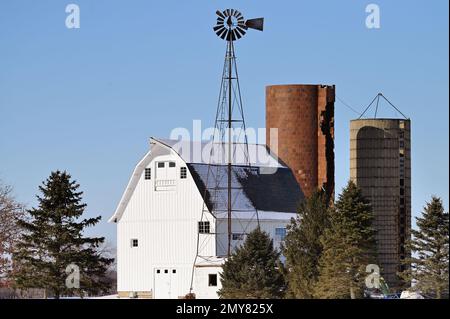 Maple Park, Illinois, USA. An einem hellen Wintertag im Nordosten von Illinois ragt eine Scheune mit Silos und Windmühlen vom Schnee ab. Stockfoto