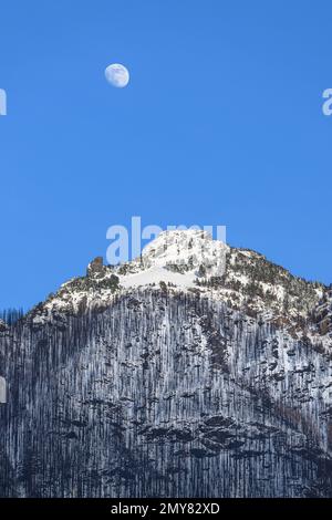 Mond in blauem Himmel über Bolt Creek Fire Brandnarbe und Cascade Mountains mit Winterschnee Stockfoto