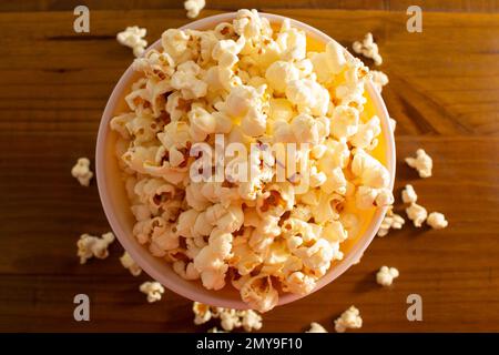 Goiania, Goias, Brasilien – 04. Februar 2023: Eine Schüssel voller Popcorn mit etwas verschüttetem Popcorn auf dem Holztisch. Stockfoto