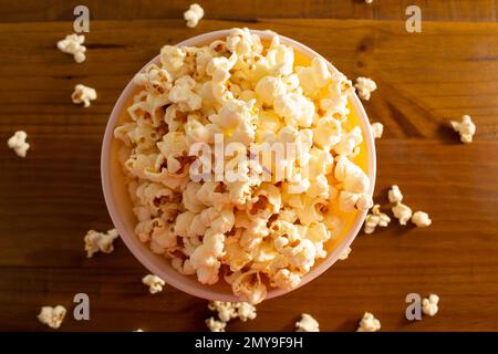 Goiania, Goias, Brasilien – 04. Februar 2023: Eine Schüssel voller Popcorn mit etwas verschüttetem Popcorn auf dem Holztisch. Stockfoto