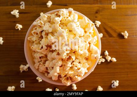 Goiania, Goias, Brasilien – 04. Februar 2023: Eine Schüssel voller Popcorn mit etwas verschüttetem Popcorn auf dem Holztisch. Stockfoto