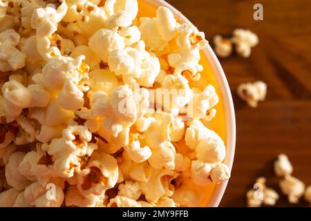 Goiania, Goias, Brasilien – 04. Februar 2023: Detail einer Schüssel voller Popcorn, wobei einige auf einem Holztisch verstreut sind. Stockfoto