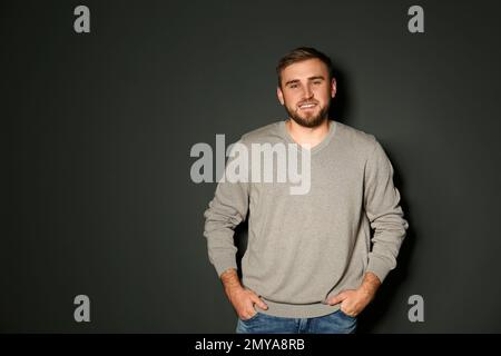 Ein hübscher Mann, der einen warmen Pullover auf dunklem Hintergrund trägt. Platz für Text Stockfoto