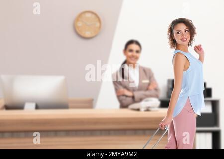 Wunderschöne Frau mit Koffer in der Nähe der Rezeption im Hotel Stockfoto