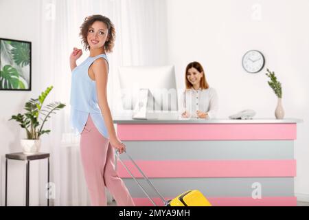 Wunderschöne Frau mit Koffer in der Nähe der Rezeption im Hotel Stockfoto