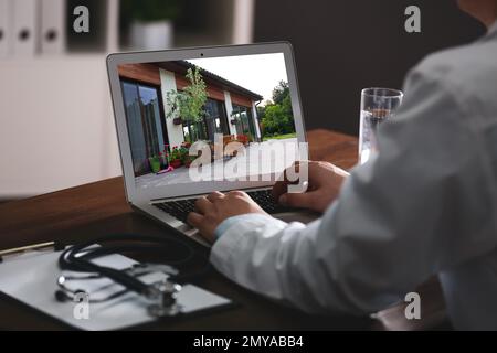 Online-Service für Immobilienmakler. Ein Arzt wählt ein neues Haus über Laptop, Nahaufnahme Stockfoto