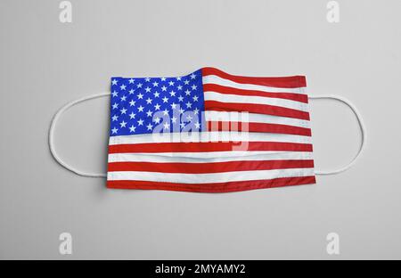 Medizinische Schutzmaske mit USA-Flaggenmuster auf hellgrauem Hintergrund, Draufsicht. Gefährlicher Virus Stockfoto