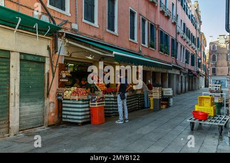 Ein Obst- und Gemüseladen mit Gemüsehändlern, die die Waren im Morgengrauen in der Sestiere von San Polo, Venedig, Veneto, Italien anordnen Stockfoto