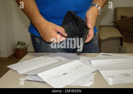 Bild eines Mannes, der ohne Geld eine Geldbörse hält und verschiedene Scheine auf dem Tisch liegen. Aktuelle Wirtschafts- und Finanzkrise. Stockfoto