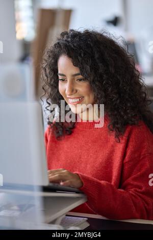 Junge, glückliche lateinische Studentin e-learning mit Laptop. Vertikaler Schuss Stockfoto