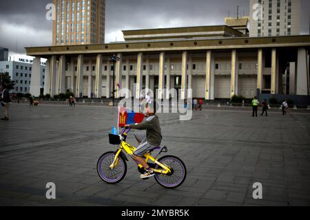 In this Sunday, July 10, 2016, file photo, a boy rides his bicycle with a Mongolian flag across Sukhbaatar Square in Ulaanbaatar. Mongolians will celebrate the anniversary of Genghis Khan's march to world conquest on July 11 with the annual Naadam sports festival featuring traditional Mongolian events including wrestling, archery, and horse racing. (AP Photo/Mark Schiefelbein, File)