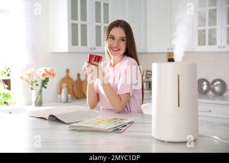 Frau, die Kaffee in der Küche trinkt, mit modernem Luftbefeuchter Stockfoto