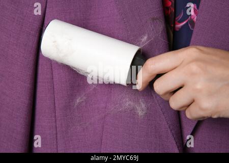 Frau, die Haare von der lila Jacke entfernt, mit Fusselroller, Nahaufnahme Stockfoto