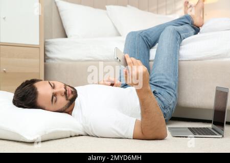 Fauler junger Mann mit Laptop und Smartphone, der zu Hause auf dem Boden lag Stockfoto