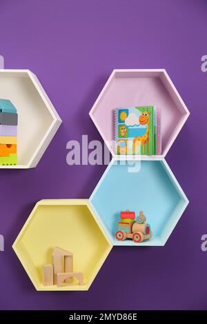 Sechseckige Regale mit Spielzeug an lila Wänden. Innendesign Stockfoto