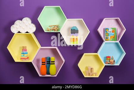 Sechseckige Regale mit Spielzeug an lila Wänden. Innendesign Stockfoto