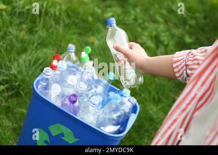 Frau, die benutzte Flaschen draußen in den Mülleimer wirft, macht dicht. Kunststoffrecycling Stockfoto