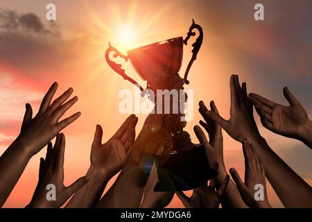 Siegerteam mit goldenem Pokal gegen die Sonne am Himmel Stockfoto