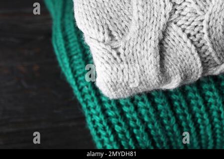 Gefaltete warme Pullover auf schwarzem Holztisch, Nahaufnahme Stockfoto