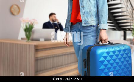 Frau mit Koffer in der Nähe der Rezeption im Hotel, Nahaufnahme Stockfoto