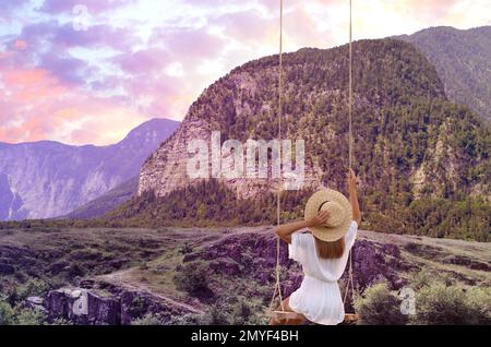 Traumwelt. Eine junge Frau, die unter dem Sonnenuntergang über den Bergen schwingt Stockfoto