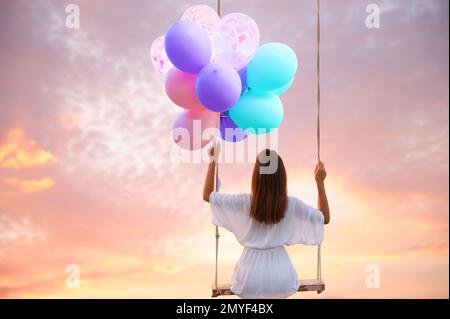 Traumwelt. Junge Frau mit hellen Ballons, die schwingen, Sonnenuntergang am Hintergrund Stockfoto