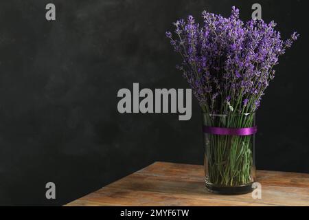 Wunderschöne Lavendelblumen in Glasvase auf Holztisch vor dunklem Hintergrund. Platz für Text Stockfoto