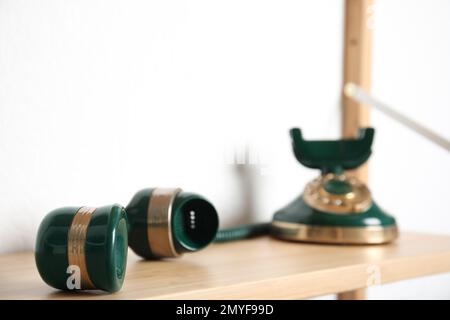 Handset und grünes, klassisches Schnurtelefon auf Holzregal in der Nähe weißer Wand, Nahaufnahme Stockfoto