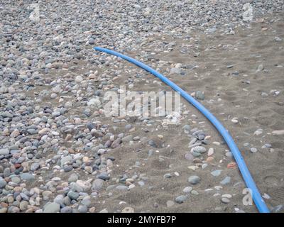 Kabel auf schwarzem Sand. Das Kabel ragt aus dem Boden heraus. Elektrische Kommunikation am Strand. Industrie. Unfertige Arbeit Stockfoto