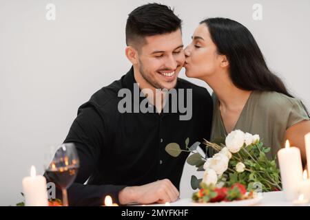Emotionale hübsche Frau, die Blumen hält und ihren hübschen Freund küsst Stockfoto