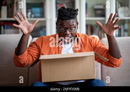 Aufgeregter, fetter afrikanischer Kunde erhält gutes Paket, Zustellung wird eröffnet Stockfoto