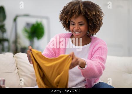 Glückliche schwarze Frau, die ihre neuen Kleider überprüft Stockfoto