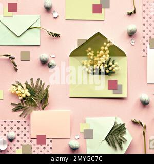 Ostern-Hintergrund. Mimosa- und Freesia-Blumen, mintgrüne Umschläge und farbiges Papier auf beigefarbenem Hintergrund. Flach liegend, über Kopf, knabbernd, ordentlich angeordnet Stockfoto