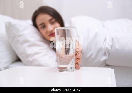 Junge Frau, die zu Hause ein Glas Wasser aus dem Nachttisch nimmt, konzentriert euch auf die Hand Stockfoto