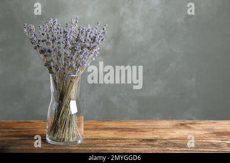 Getrocknete Lavendelblumen in Glasvase auf Holztisch vor grauem Hintergrund. Platz für Text Stockfoto