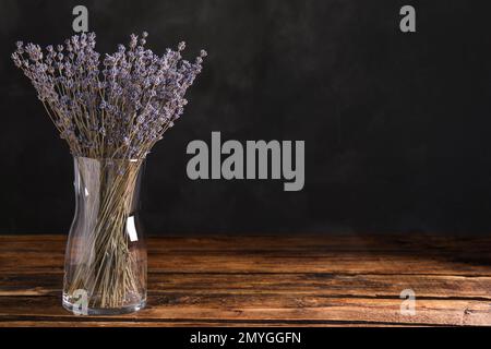 Getrocknete Lavendelblumen in Glasvase auf Holztisch vor dunklem Hintergrund. Platz für Text Stockfoto