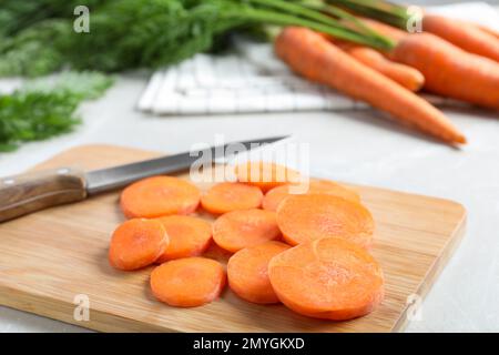 Holzbrett mit Karottenscheiben und Messer auf hellgrauem Marmortisch, Nahaufnahme Stockfoto