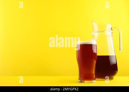 Köstlicher hausgemachter Kvass in Glas und Kanne auf gelbem Hintergrund. Platz für Text Stockfoto