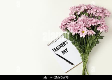 Blumen und Notizbuch mit Wörtern LEHRERTAG auf weißem Hintergrund, flach liegend. Platz für Text Stockfoto