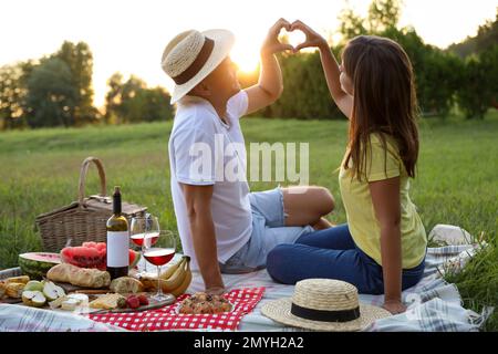 Ein glückliches Paar, das ein Herz mit einem praktischen Picknick im Park macht Stockfoto