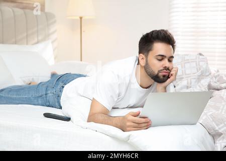 Fauler junger Mann mit Laptop im Bett zu Hause Stockfoto