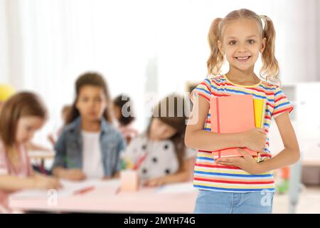 Glückliches kleines Mädchen mit Notizbüchern im Klassenzimmer Stockfoto