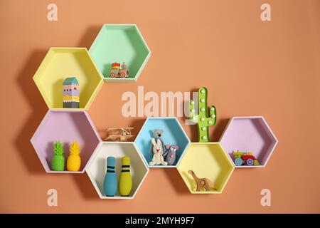 Sechseckige Regale mit Spielzeug an orangefarbenen Wänden. Innendesign Stockfoto